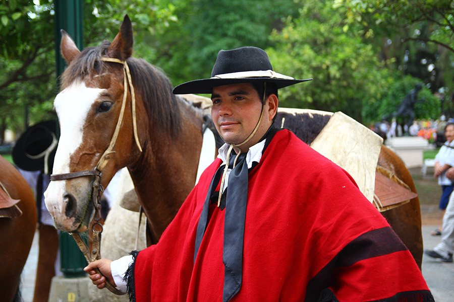 Lokalny mieszkaniec Argentyny w czerwonym stroju trzyma konia za wodze