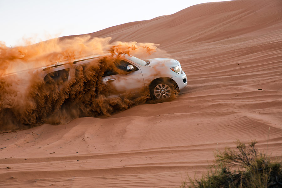 Białe auto sunące po pustyni w kłębie piasku - Ecco Travel, Ras Al Khaimah